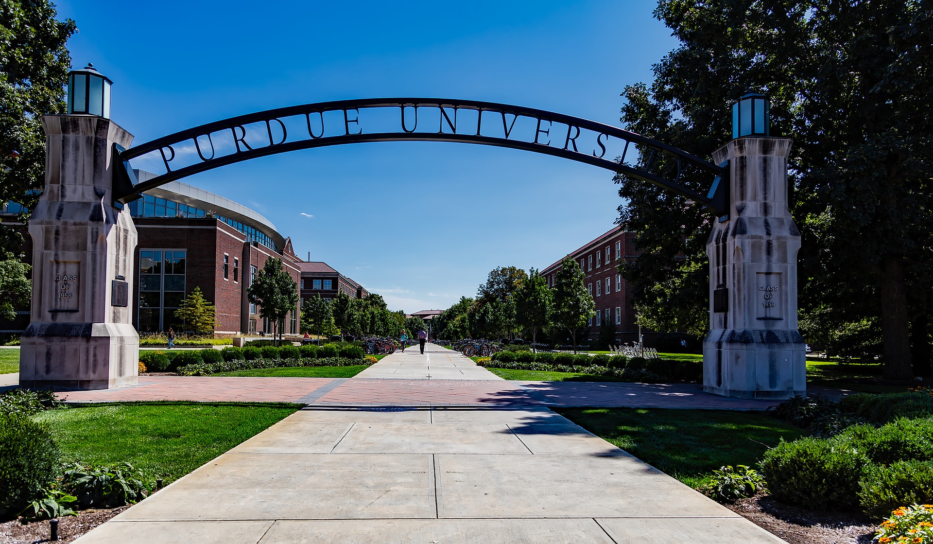 A person walking on the sidewalk under an arch.